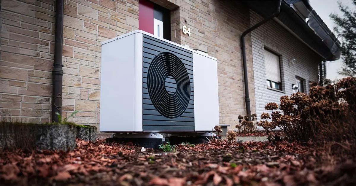 Außeneinheit einer modernen Wärmepumpe an einem weißen Wohnhaus